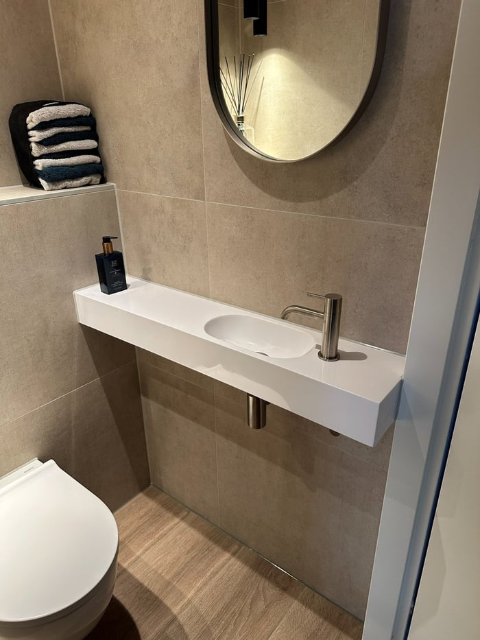Zwevende witte maatwerk fontein met rvs kraan en ovale spiegel met zwarte rand in de toiletruimte op de benedenverdieping.