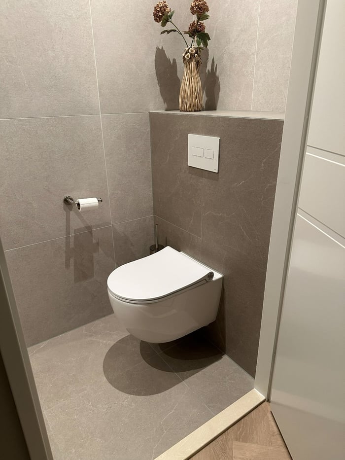 Toilet met hangend toilet, beige steenlook-tegels en droogbloemen op een nis.