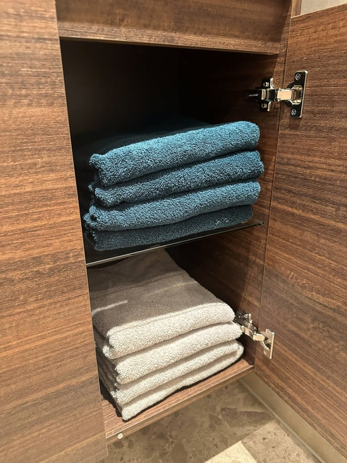 Open walnoten kast met netjes gevouwen handdoeken in blauw en zandtinten.
