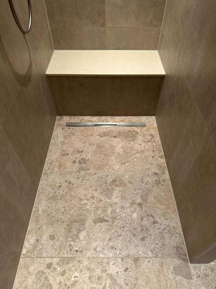 Terrazzo douchevloer met afschot naar een rvs douchegoot en een natuurstenen zitbank.