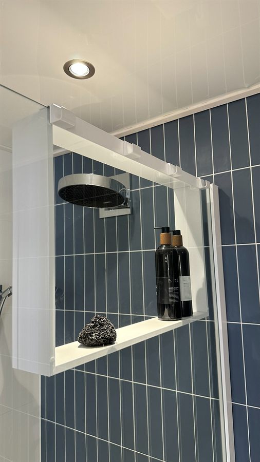 Diepblauwe tegels met een wit planchet dat over de glazen douchewand hangt